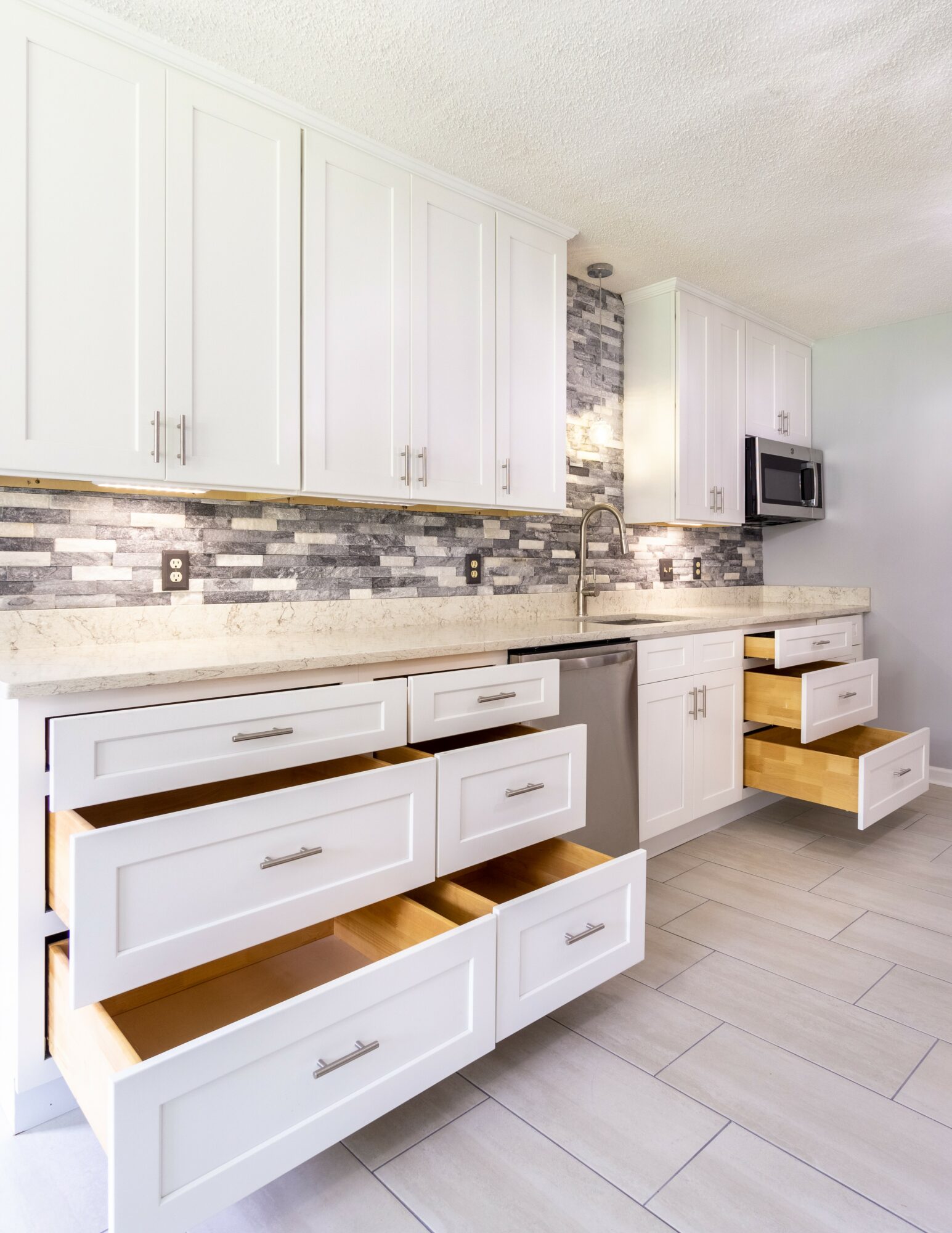 Kitchen with white cabinets, gray backsplash, and open drawers showing wooden interiors.