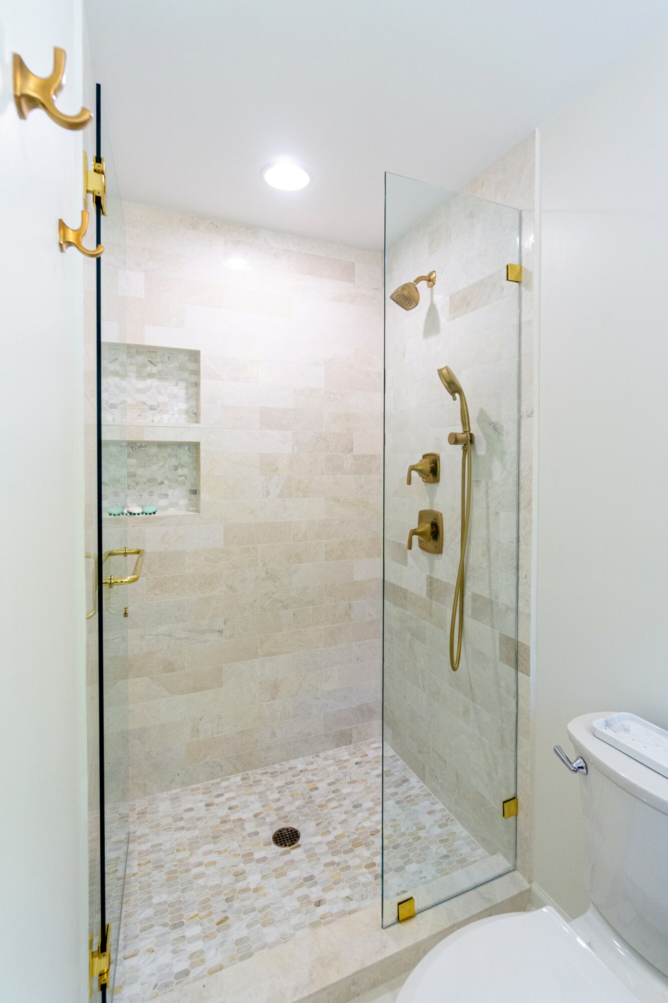 Shower area with glass door, beige tiled walls, and gold fixtures, next to a white toilet in a bathroom.