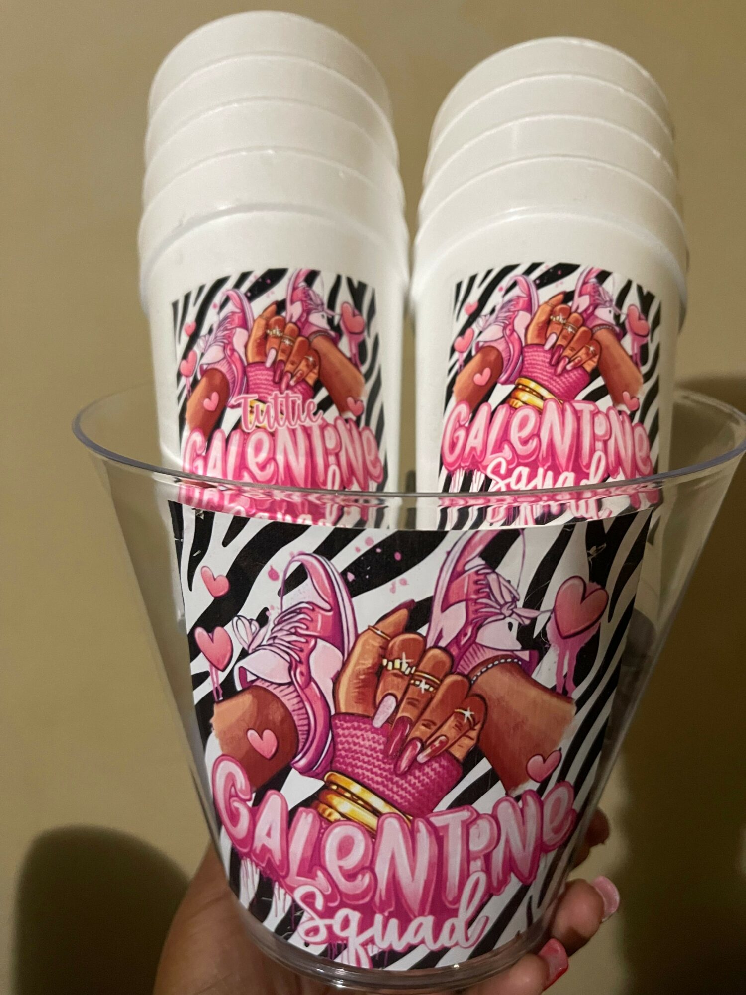 Stacked paper cups with pink, white, and black zebra pattern and Valentine's Day themed text and illustrations.