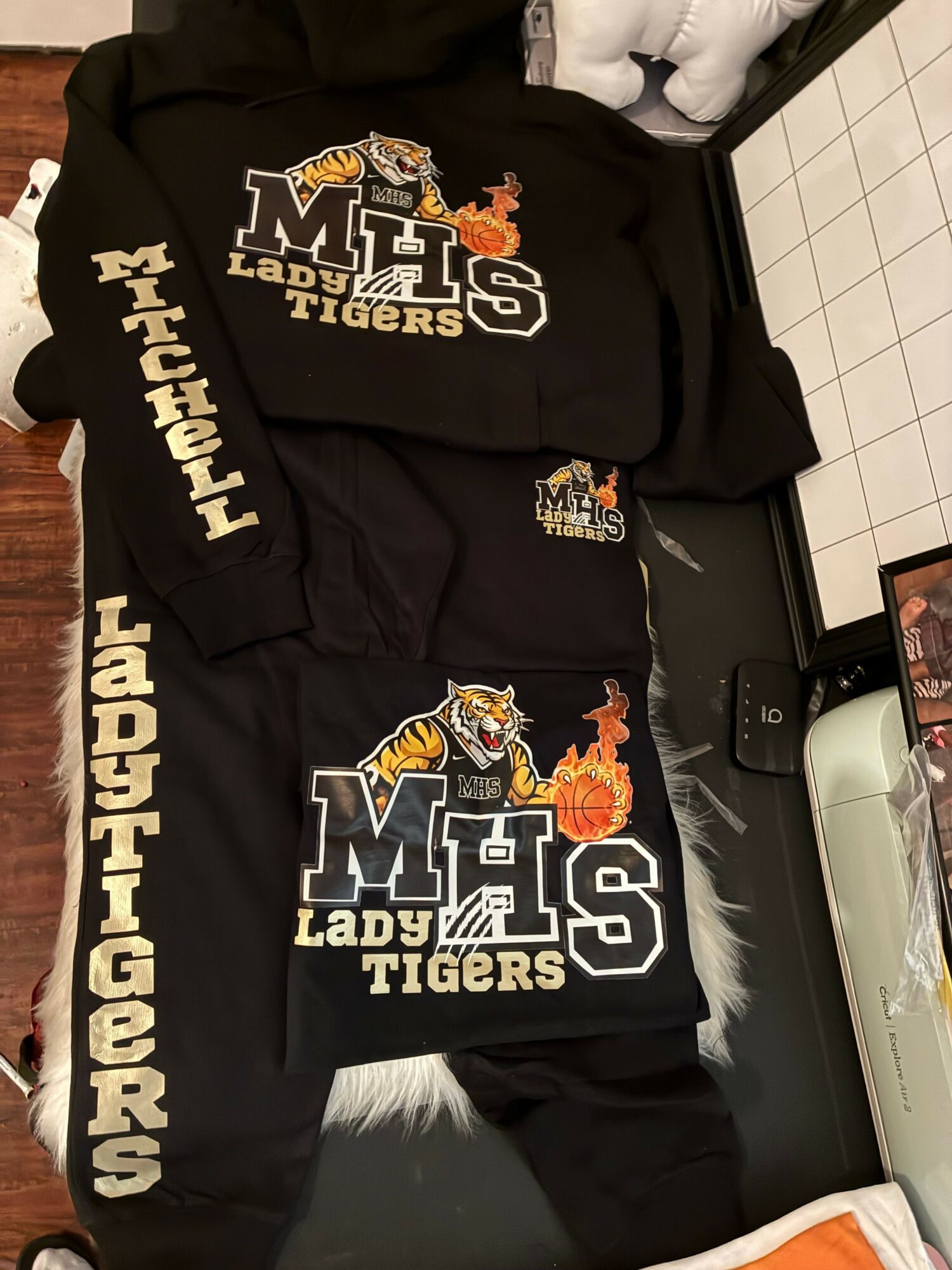 Two black hoodies with Michigan Lady Tigers logos and text, placed on a surface with a tiled wall in the background.