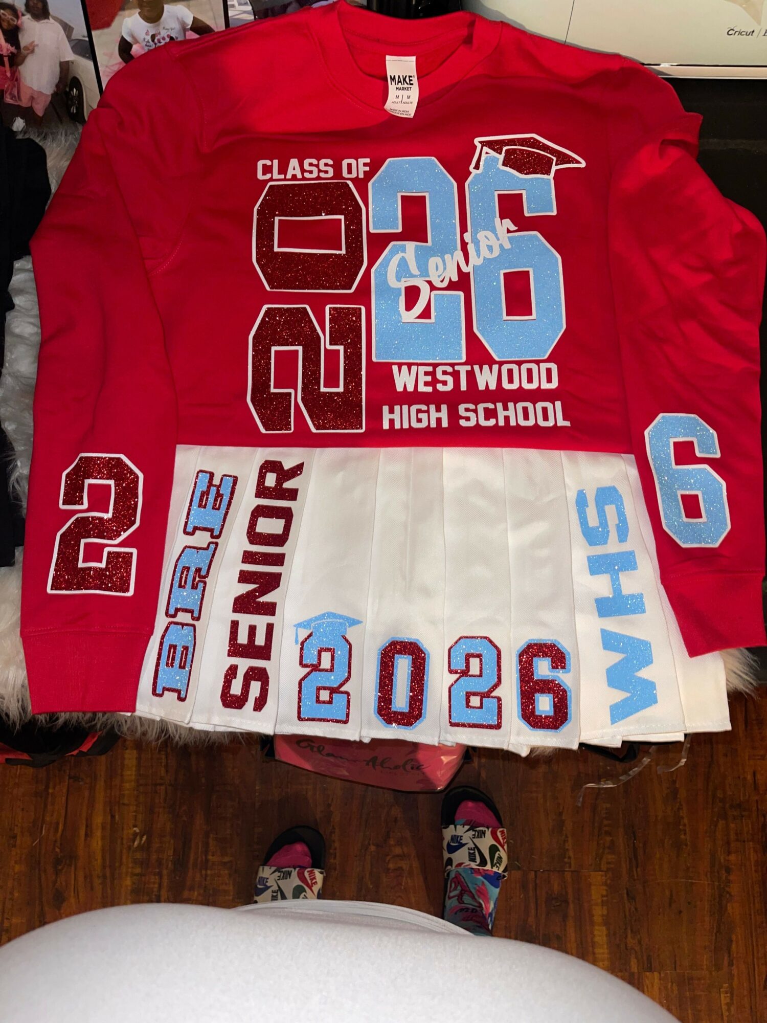 Red and white high school senior sweatshirt with large numbers and text, laid on a wooden surface.