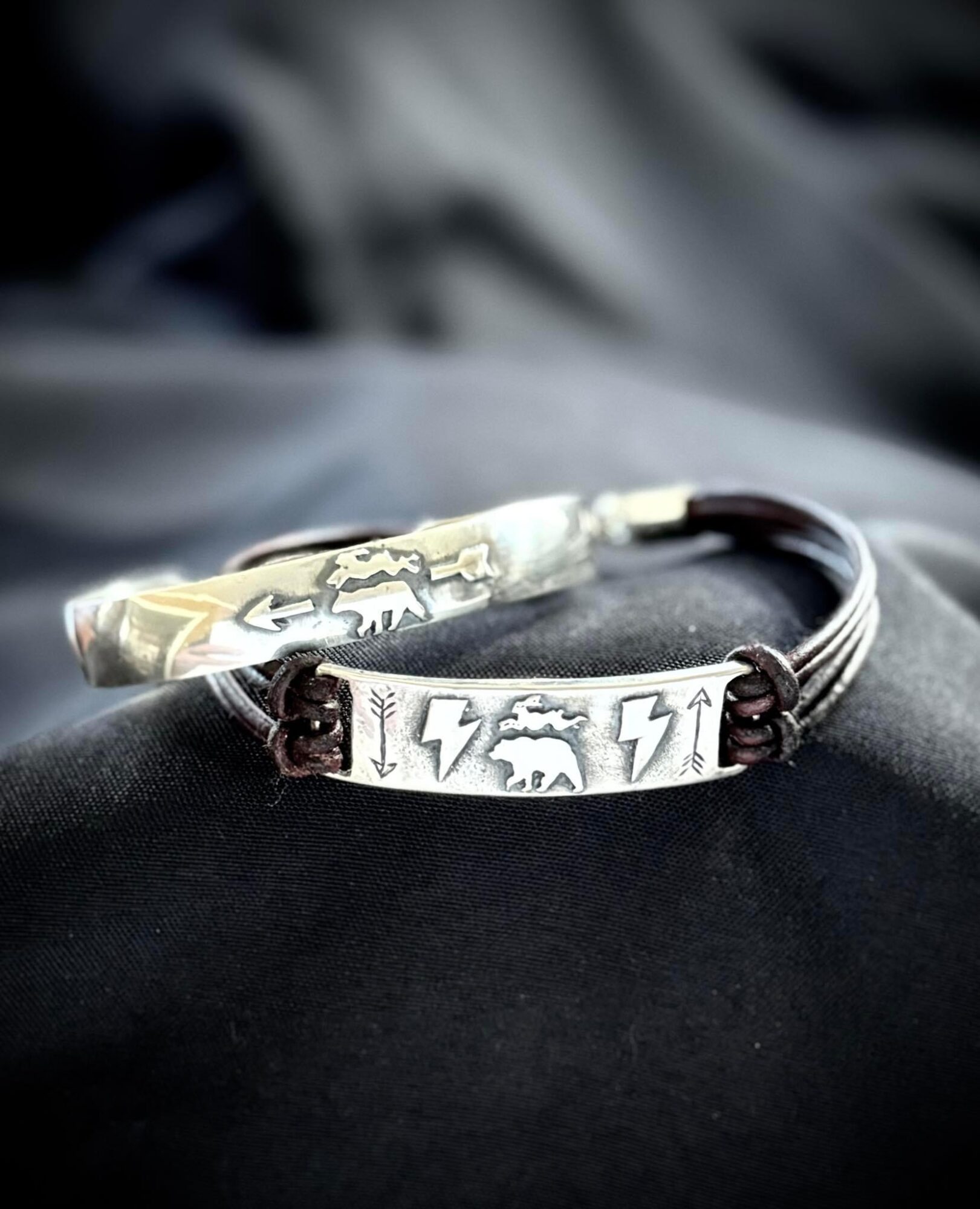 Bracelet with metal plate featuring lightning bolt and animal designs, on a dark fabric background.