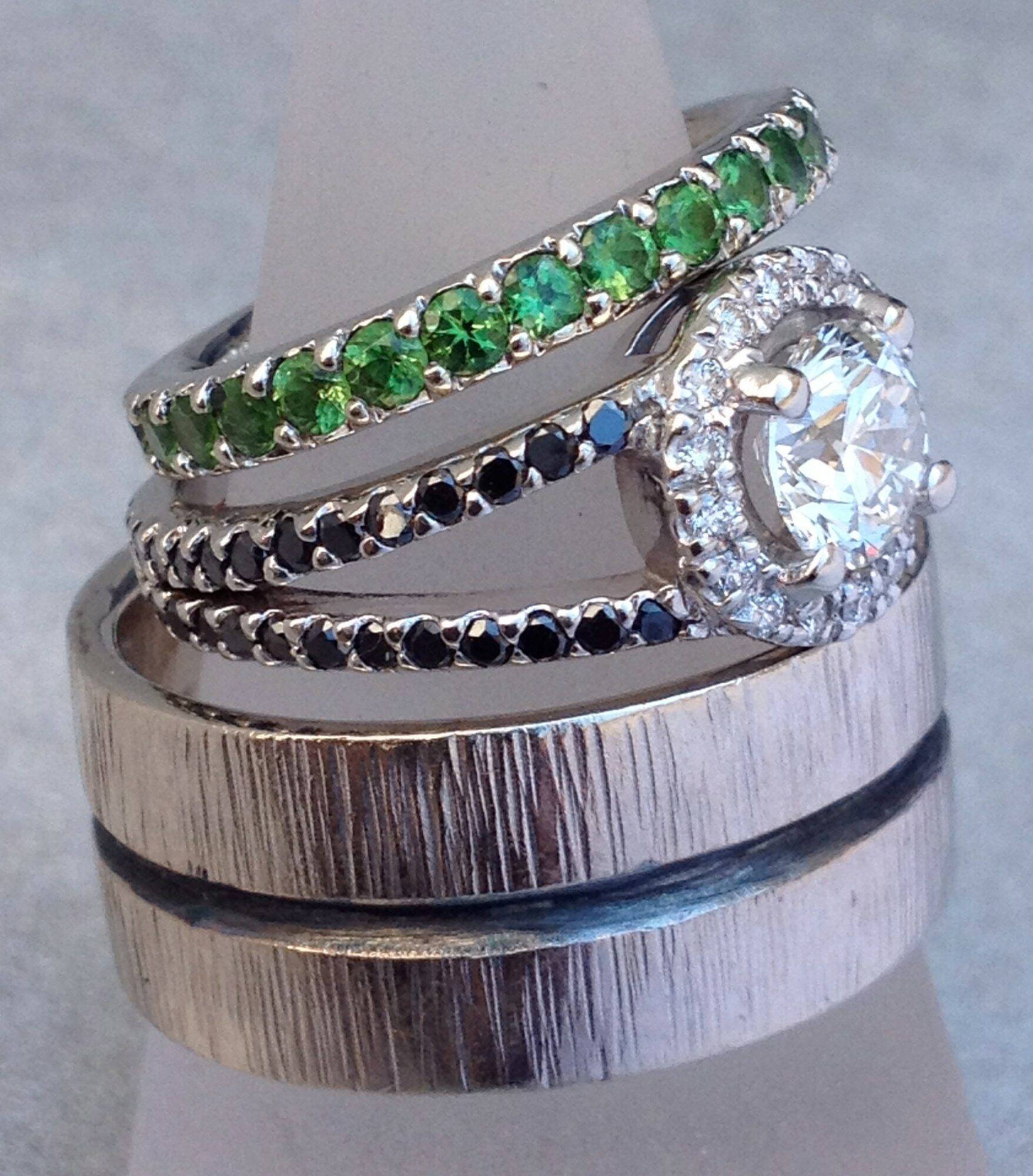 Stacked rings with green, black, and clear stones, and plain metal bands, on a gray background.