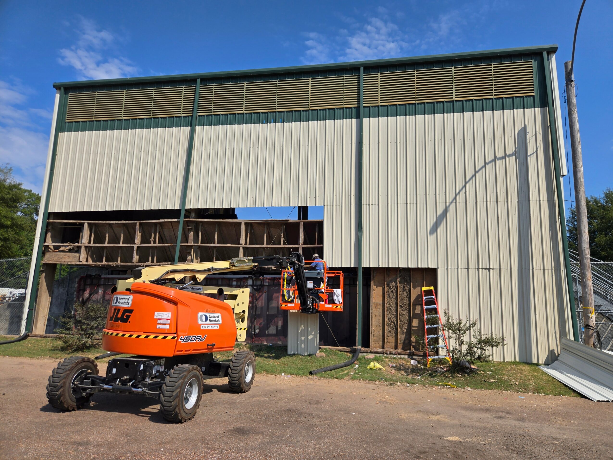 Construction site with a large building, orange lift, and construction equipment outdoors under a blue sky.