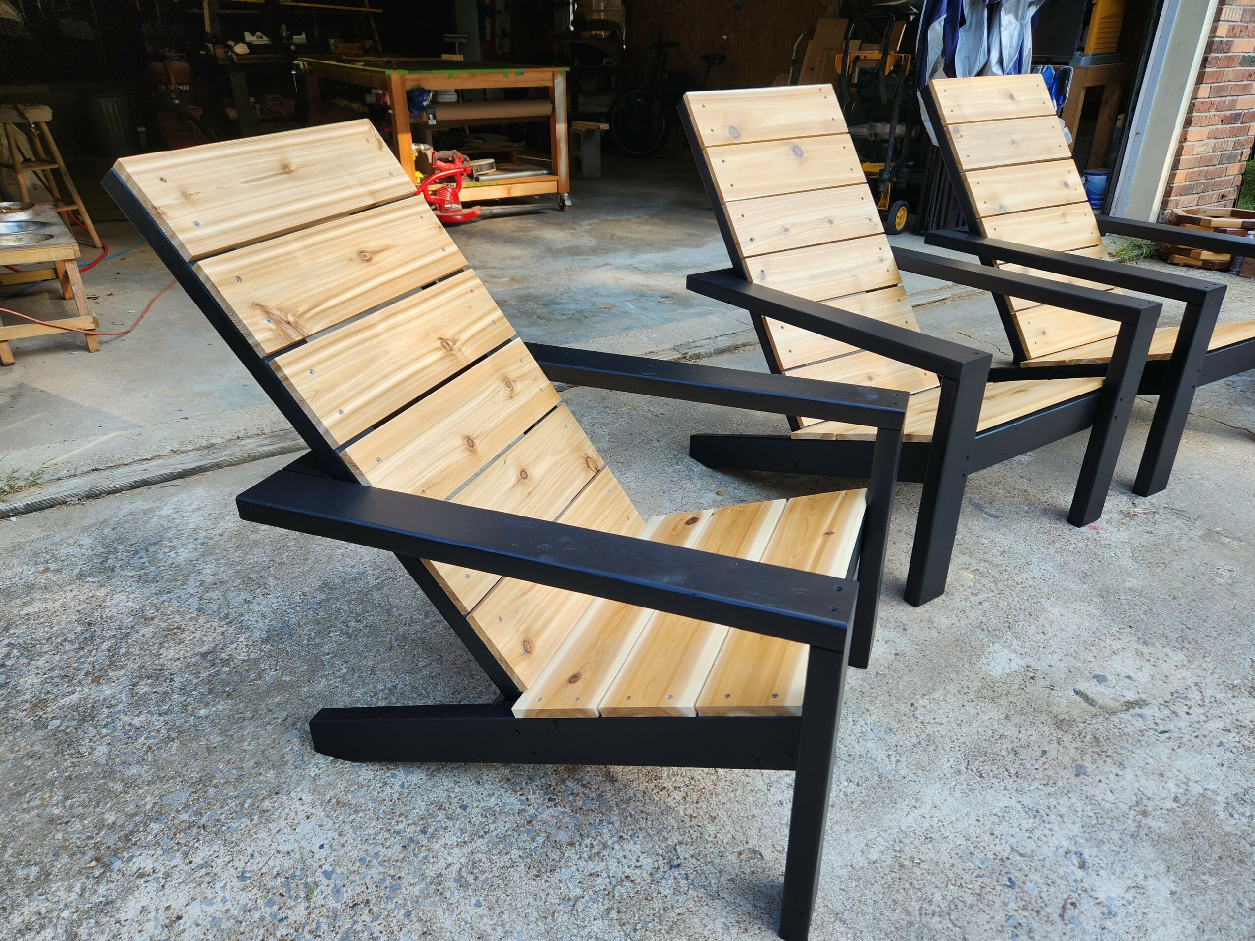 Three wooden and black metal chairs with angled backrests and armrests, arranged in a row on a concrete floor.