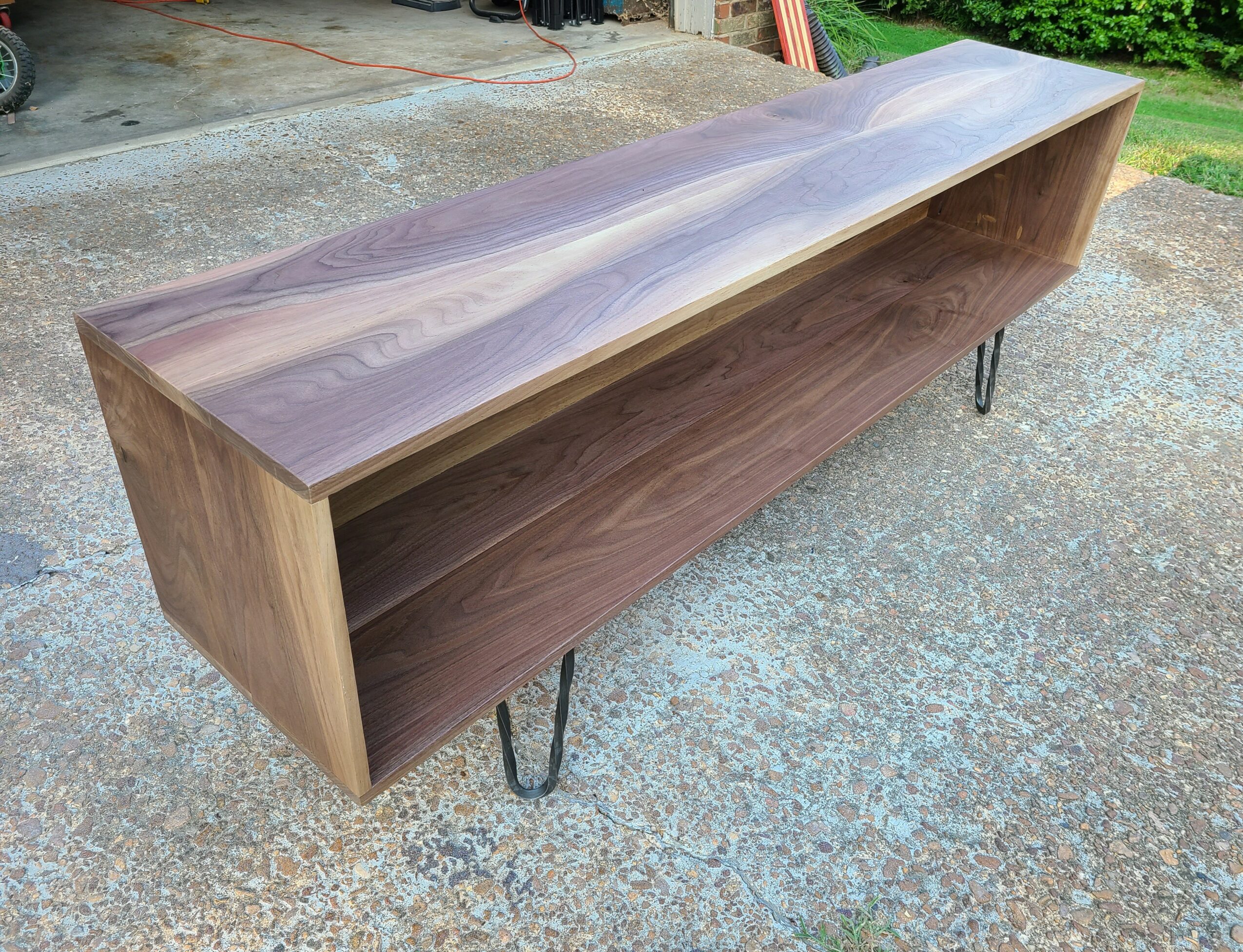 Long wooden table with metal hairpin legs on a concrete surface outdoors.