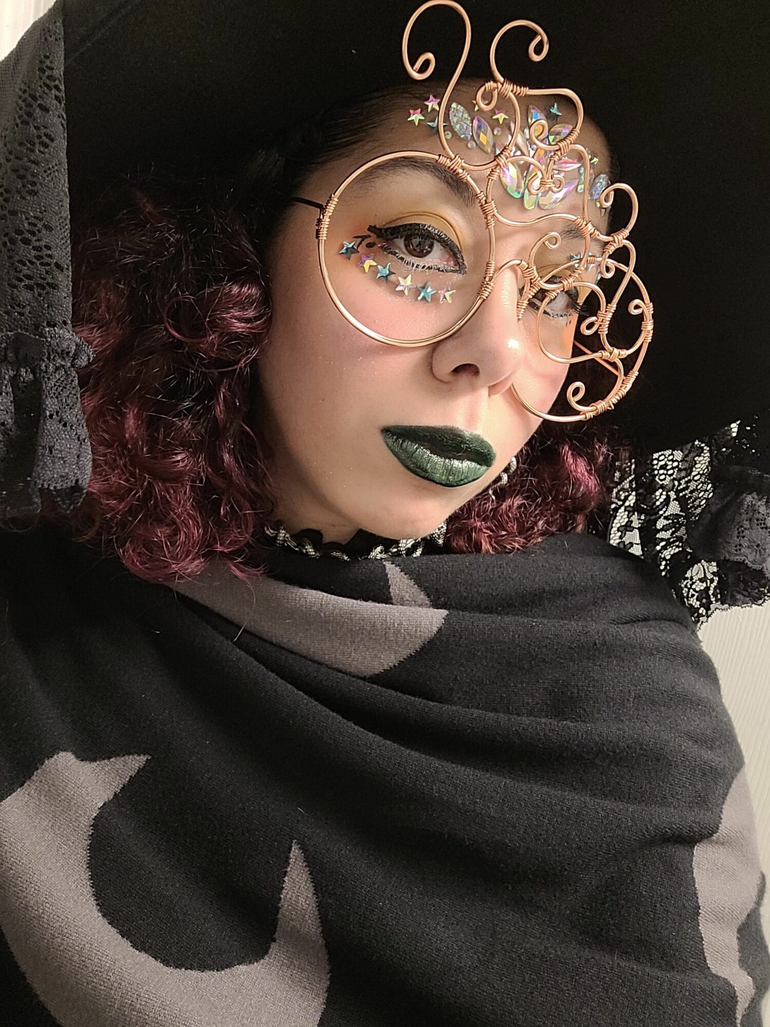 Person with curly hair, wearing glasses with decorative frames, green lipstick, and a striped garment, lying down.