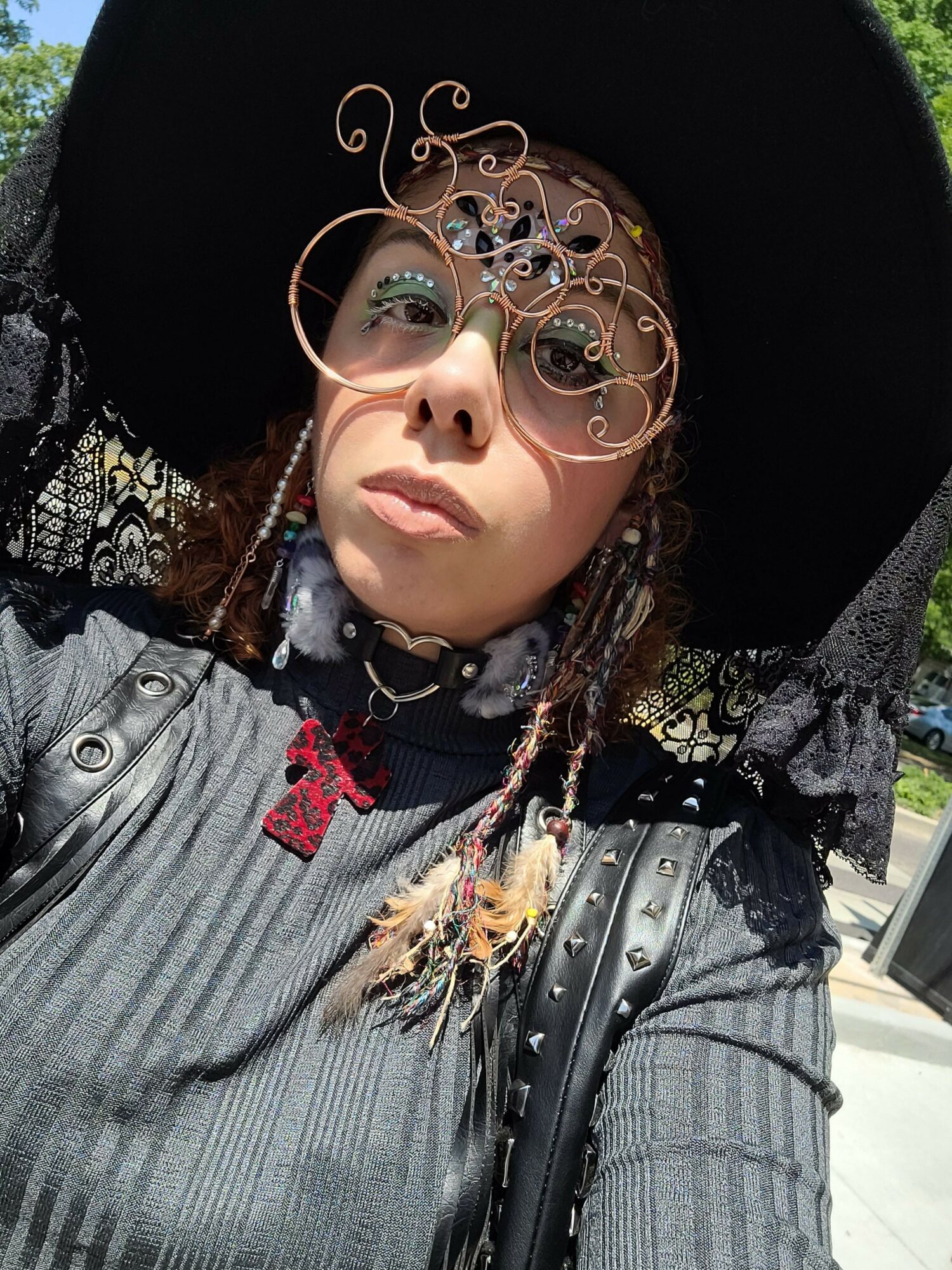 Person wearing a large black hat, gray striped jacket, and braided hair with beads, looking at the camera.