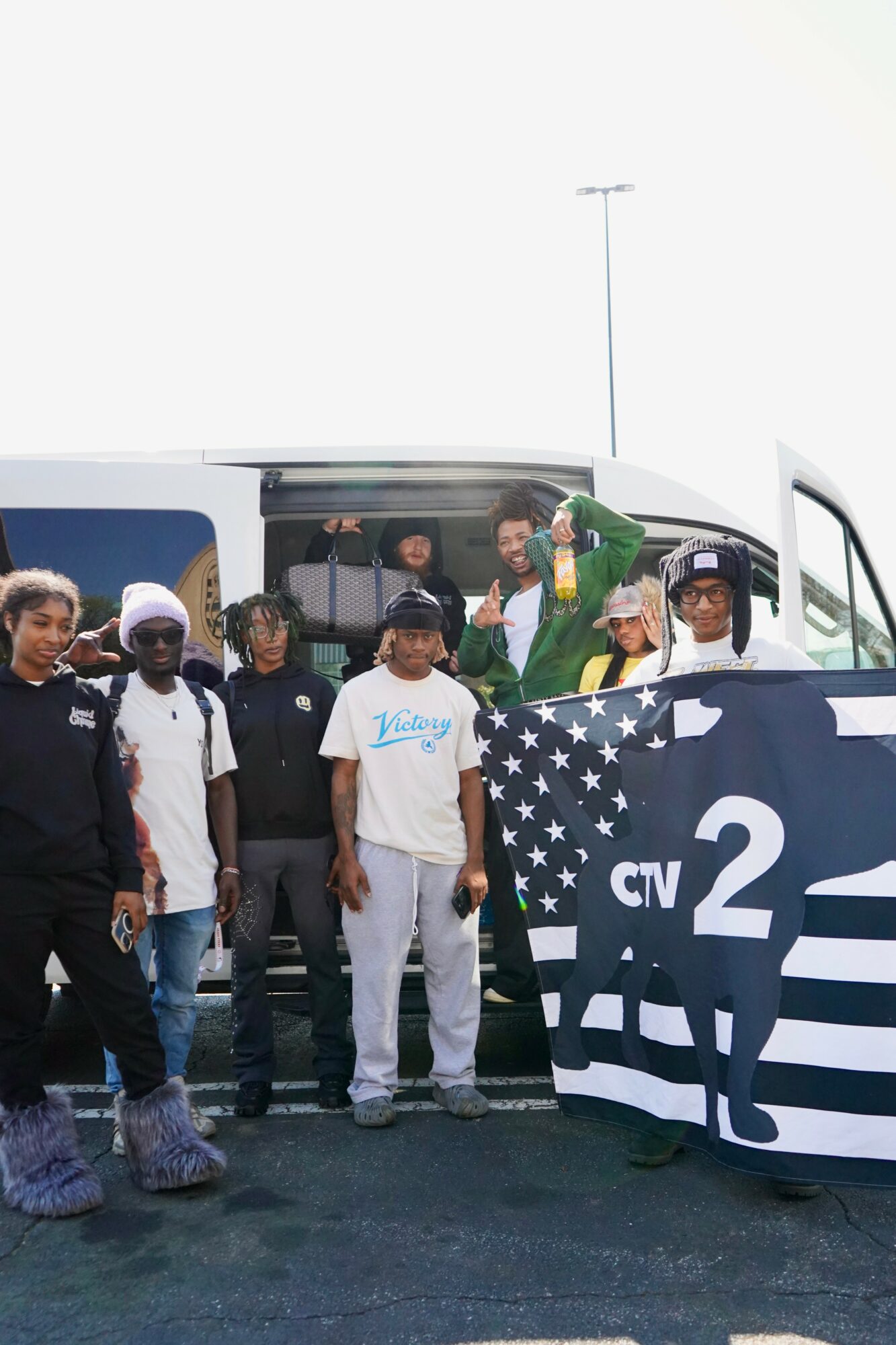 Group of people standing in front of a bus with a large American flag design, some waving and smiling.