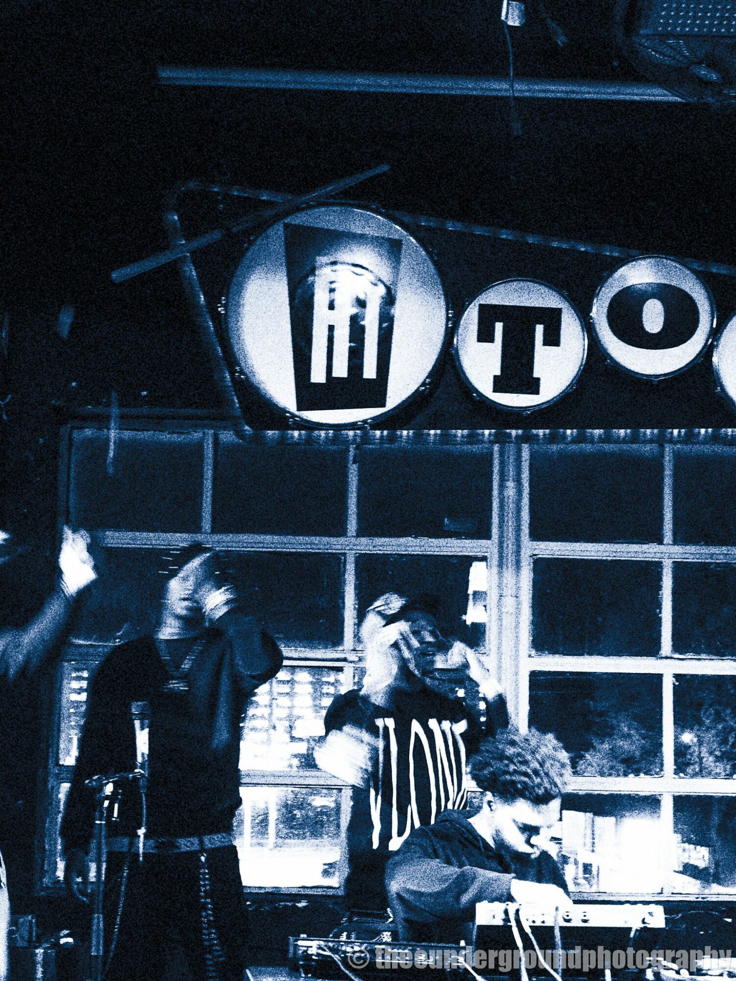 People standing near a bar or counter with a sign reading 'TO' above them, in a dark setting.