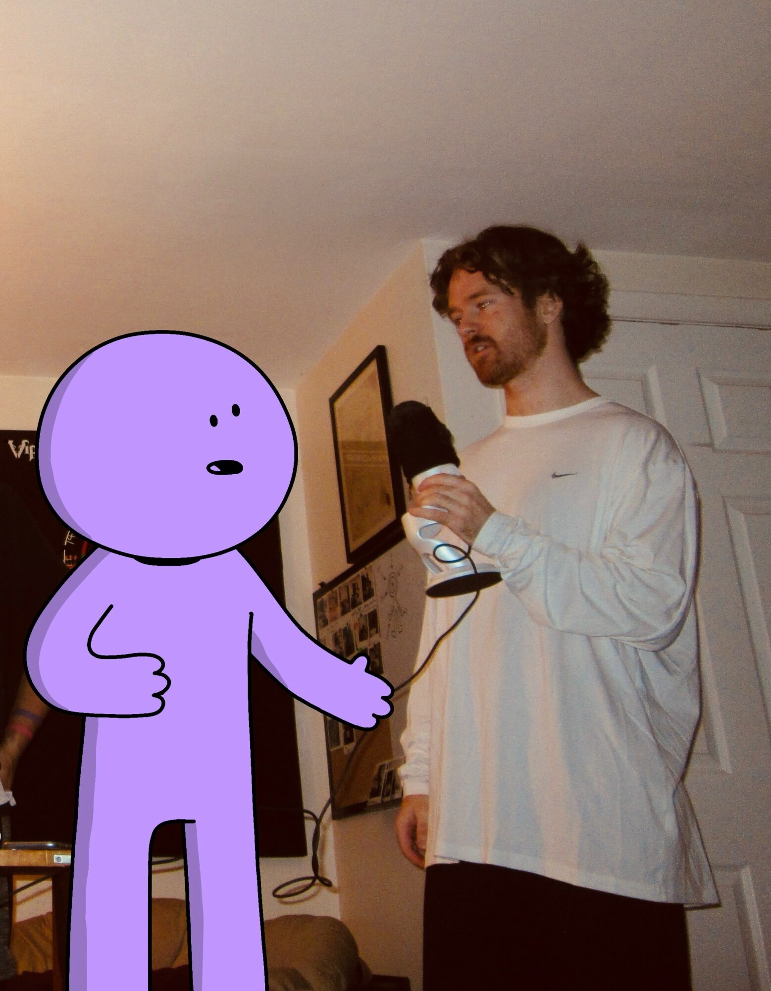 A person with curly hair and a beard wearing a white long-sleeve shirt holding a glass, standing in a room.