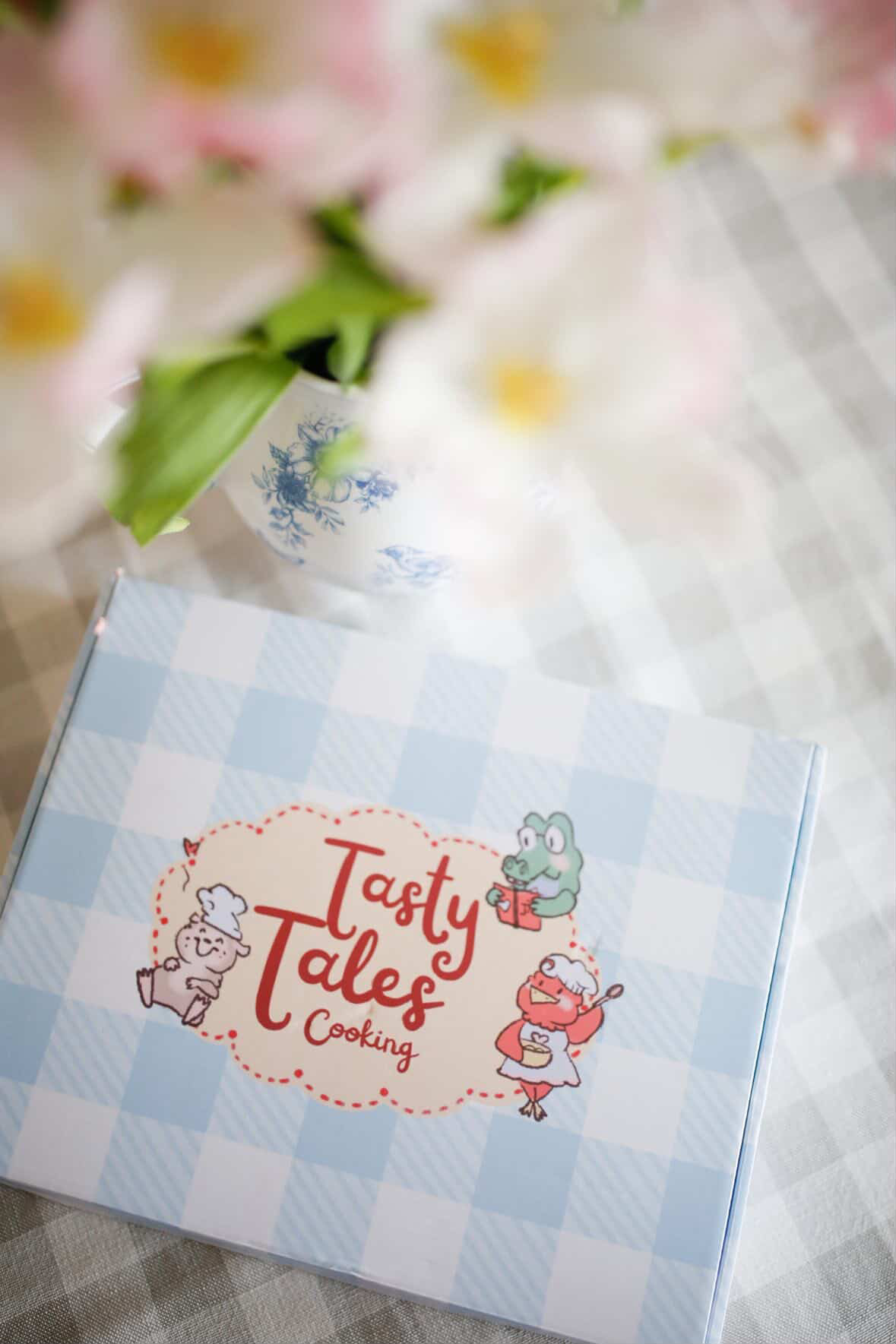 Box with cartoon characters and text 'Tasty Tale' on a checkered tablecloth.