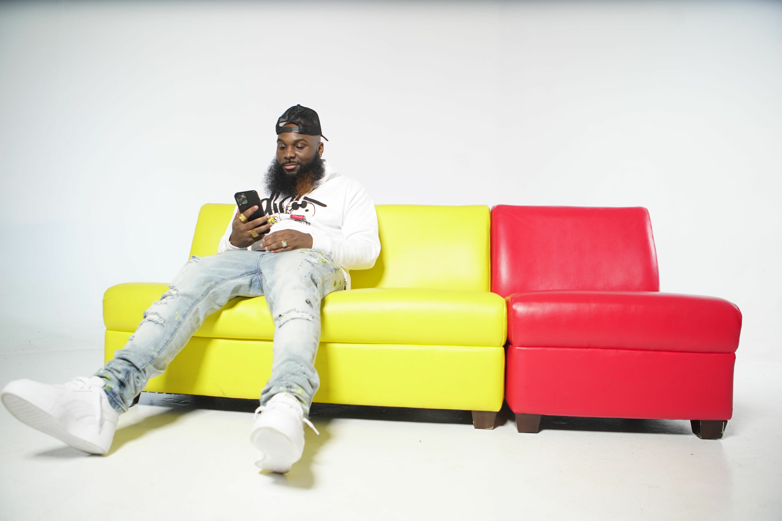 Person sitting on a yellow and red sofa, looking at a phone, against a plain white background.
