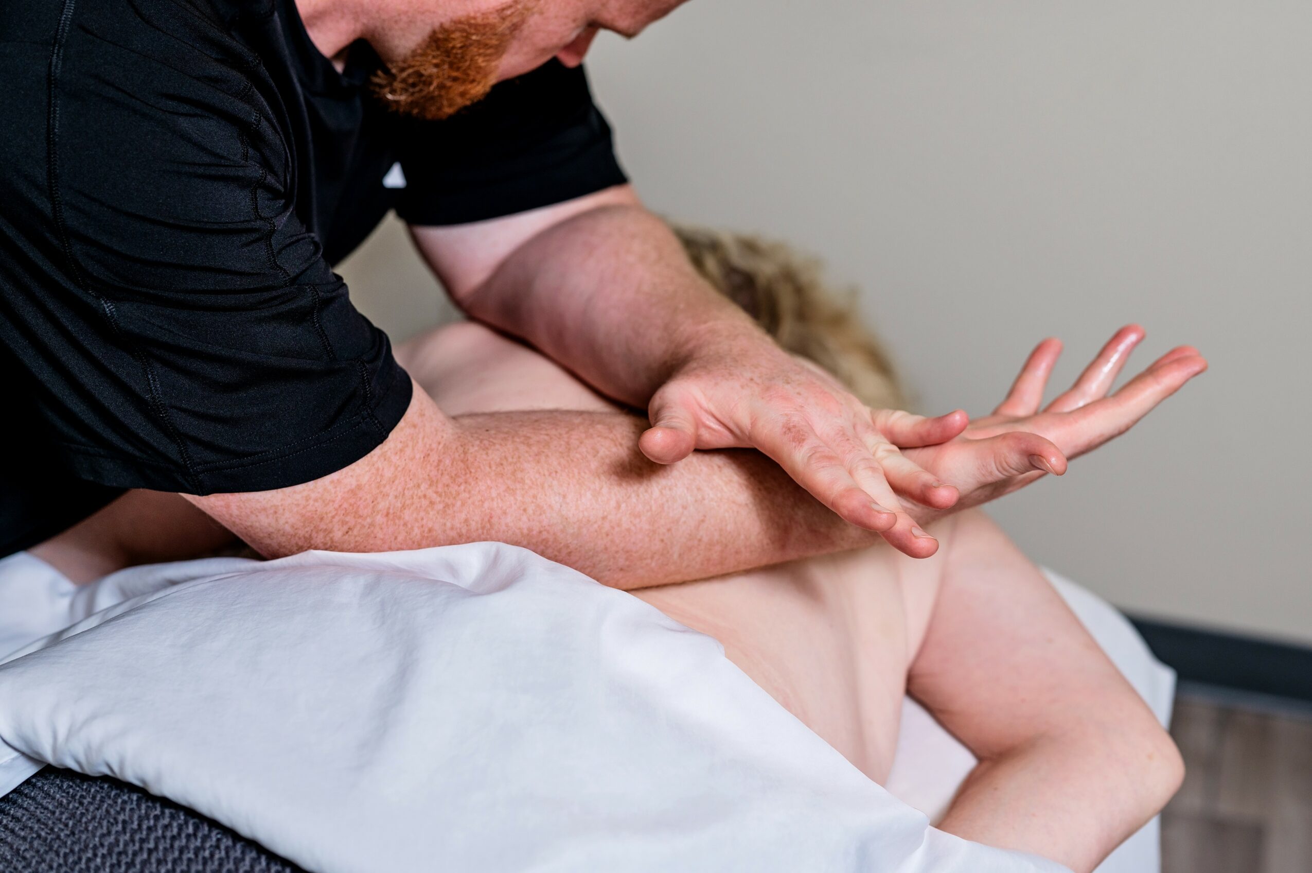 Person receiving a massage on their back, with a massage therapist applying pressure to their shoulder area.