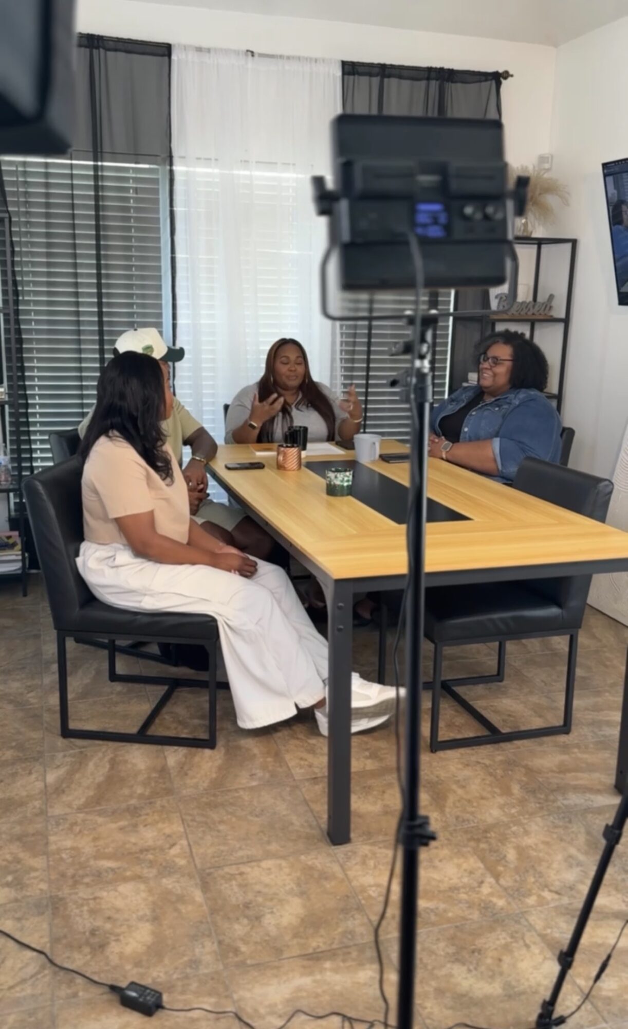 Four people sitting around a table in a room with large windows and a TV on the wall.