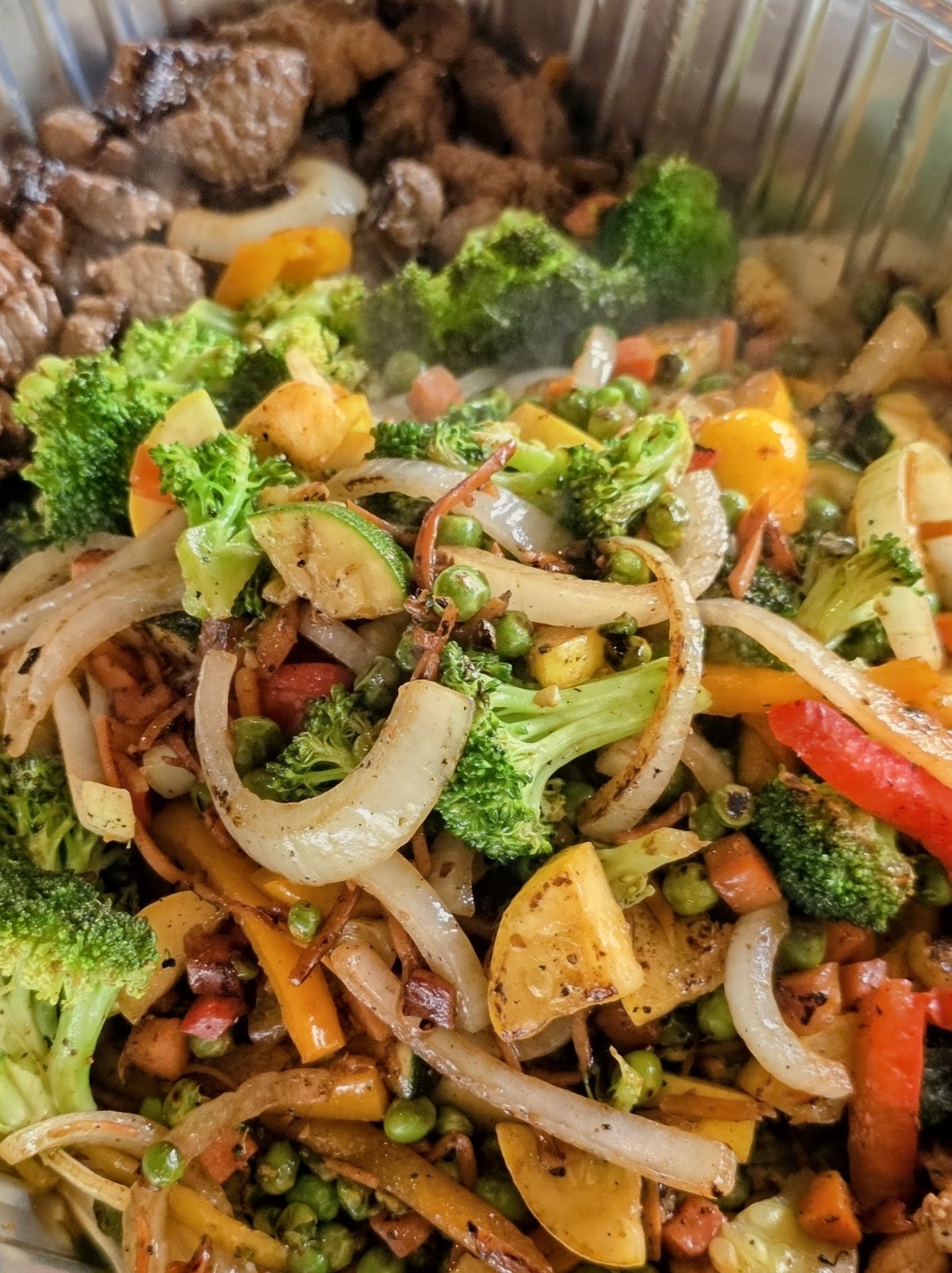 Mixed vegetable stir-fry with broccoli, red and yellow bell peppers, onions, and carrots, served in a container.
