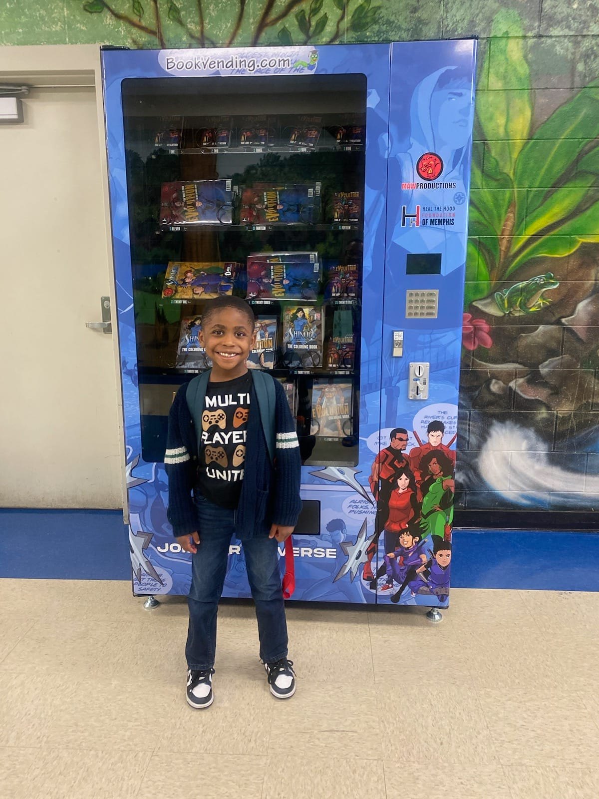 Child standing in front of a blue vending machine with colorful characters, smiling, indoors.