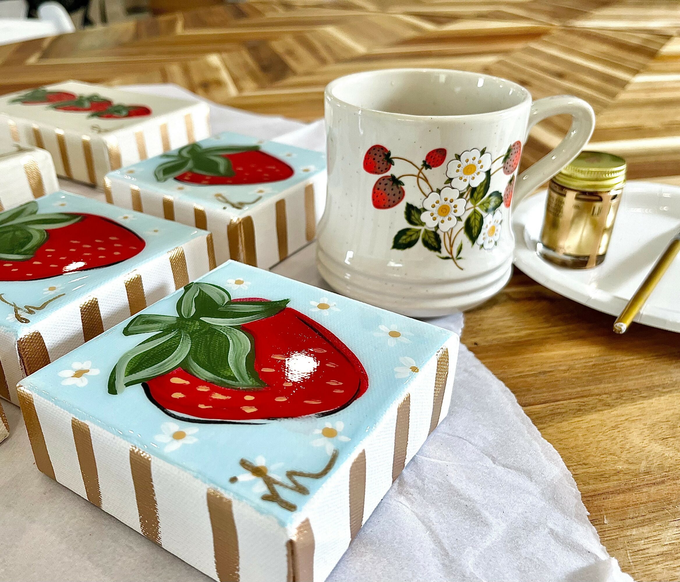 Decorated gift boxes with strawberry and floral designs, a white mug with flowers, a small jar, and a gold pen on a wooden table.