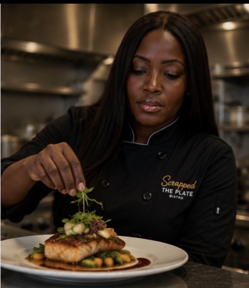 Woman in chef's uniform garnishing a plated dish in a professional kitchen, with a focused expression.