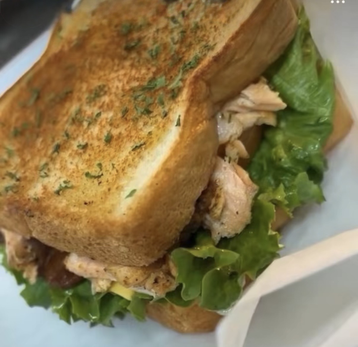 Close-up of a sandwich with toasted bread, lettuce, and chicken, on a white plate.