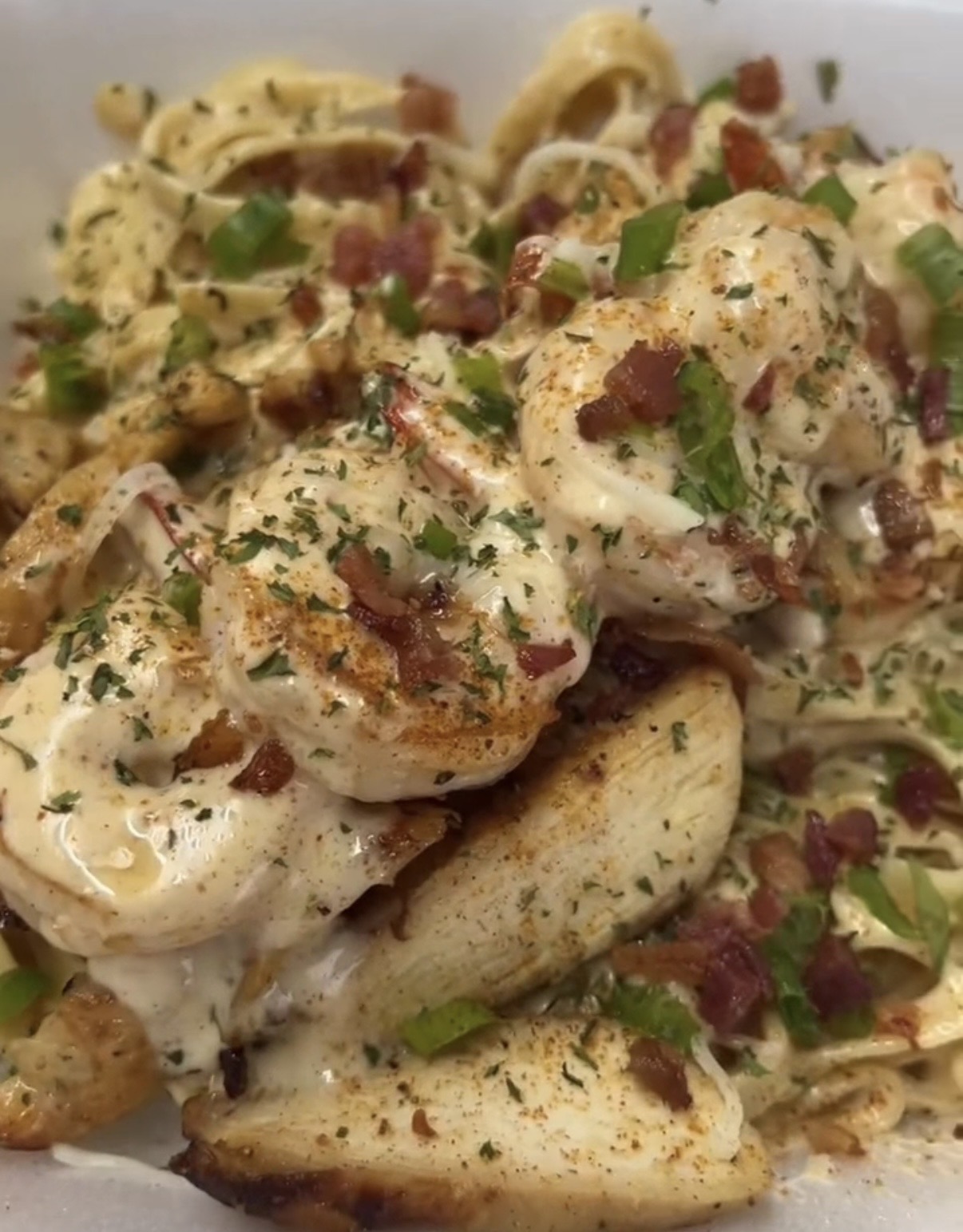 Close-up of cooked shrimp with bacon bits, green onions, and herbs on a white plate.