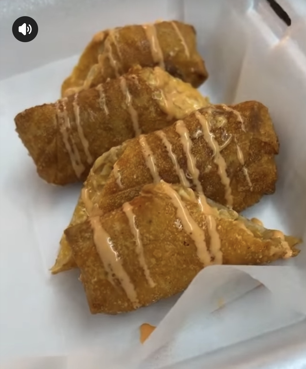 Three fried fish fillets drizzled with sauce on white paper, crispy and golden brown.