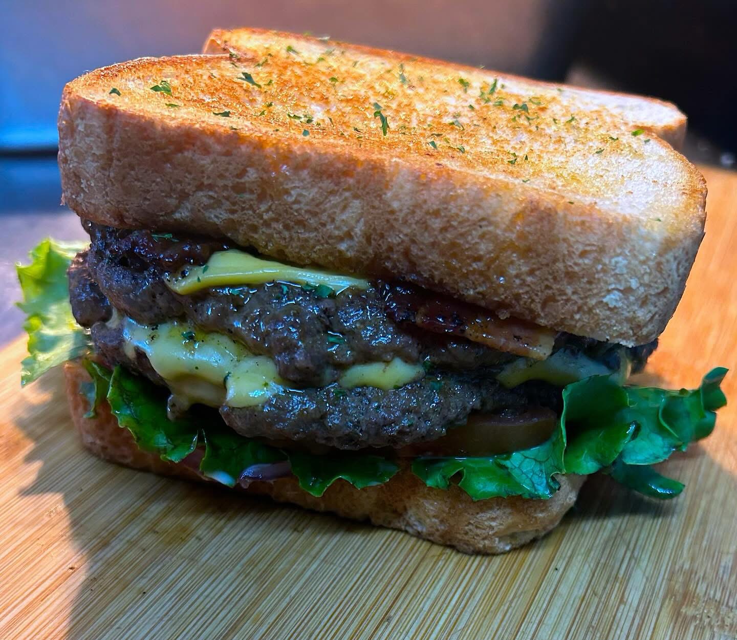 Close-up of a double cheeseburger with lettuce, cheese, and beef patties on toasted bread, on a wooden surface.