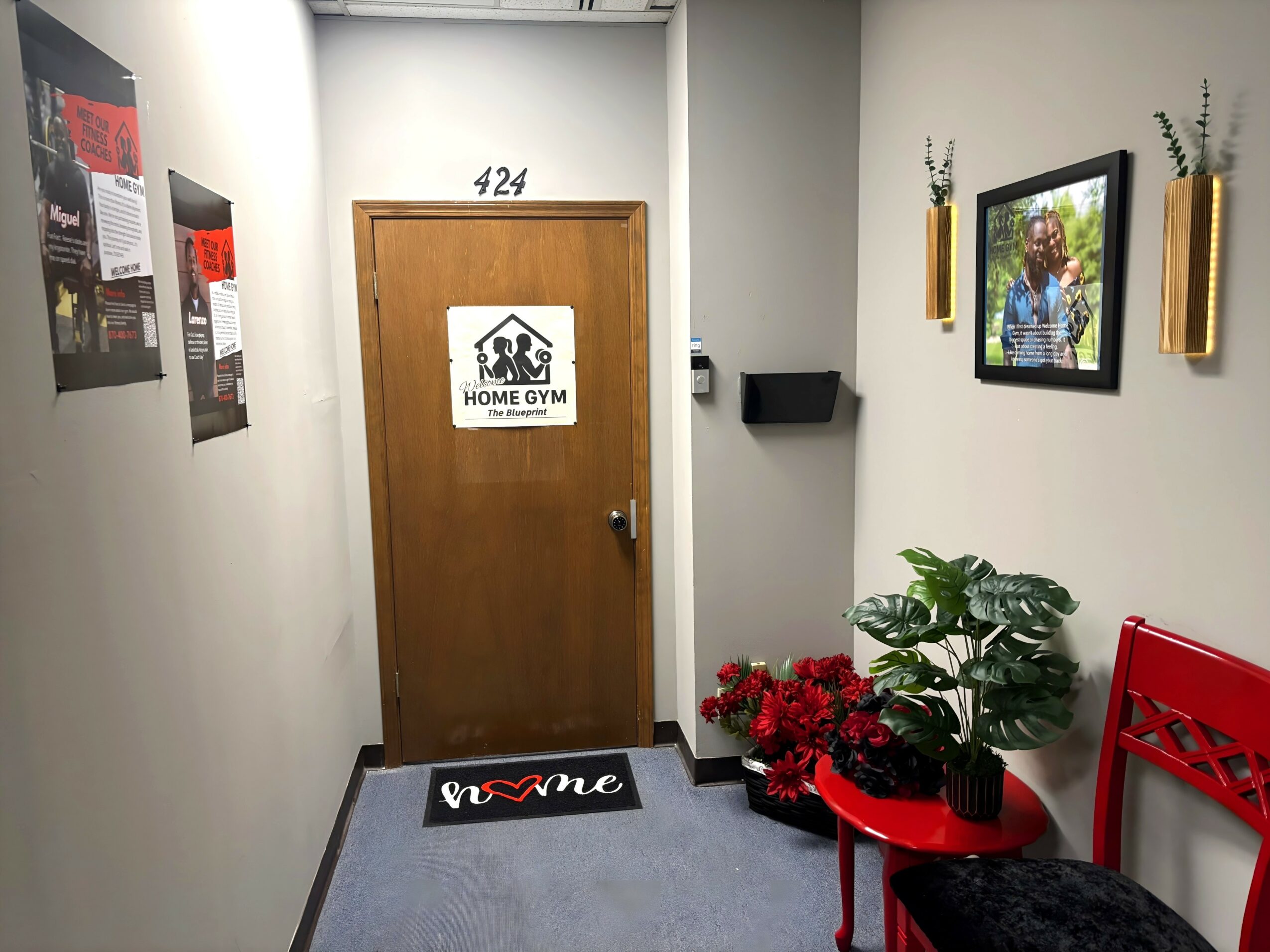 Hallway with door labeled 424, home gym sign, wall decorations, potted plant, red chair, and framed picture.