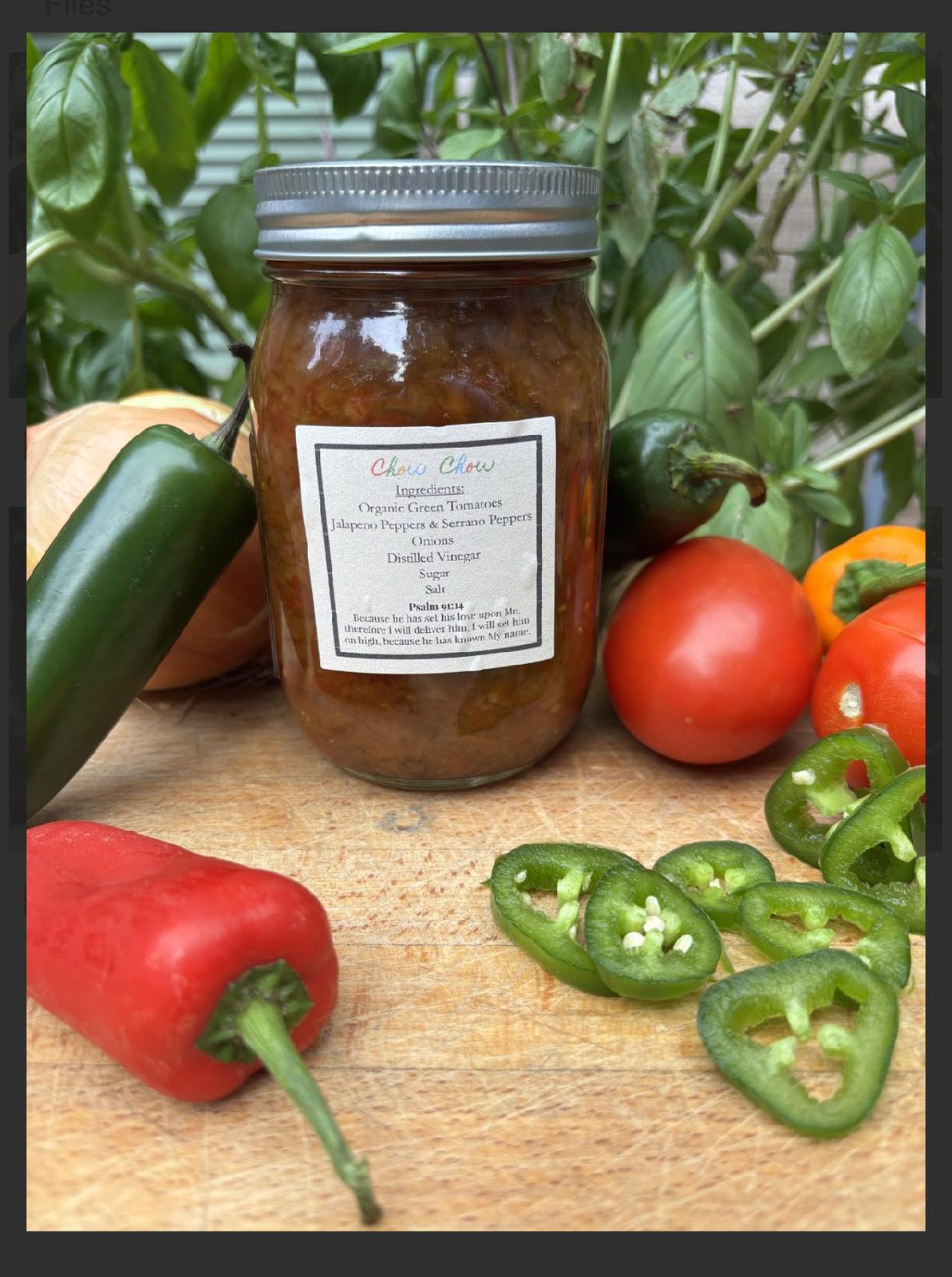 Jar of preserved food surrounded by vegetables including cucumber, tomatoes, red bell pepper, and sliced green peppers on a wooden surface.