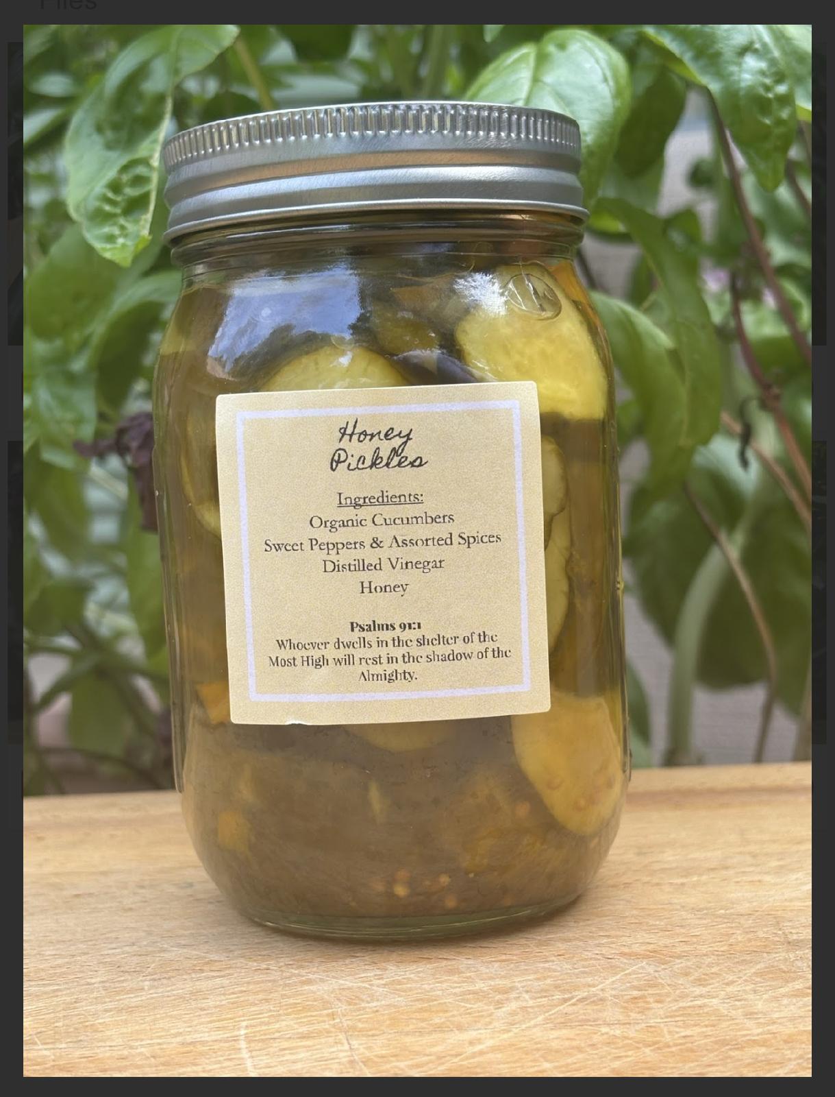Jar of honey pickles with lemon slices and spices on a wooden surface, green leaves in background.